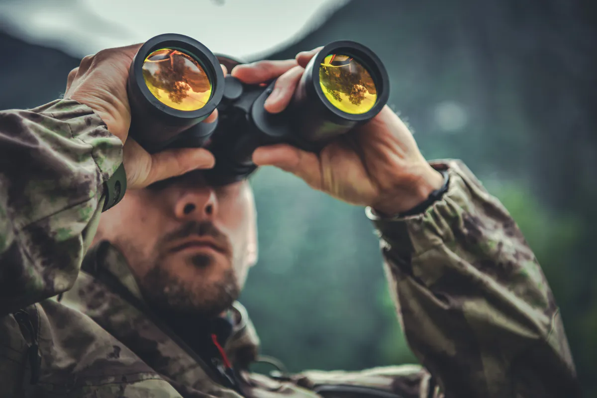A hunter glassing a distant landscape through binoculars